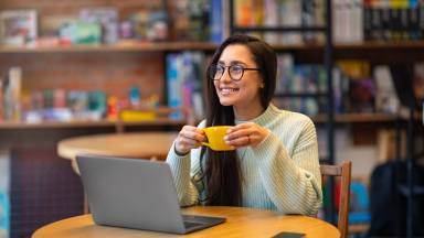 mujer-sosteniendo-un-vaso-sentada-en-una-mesa-con-una-laptop.png